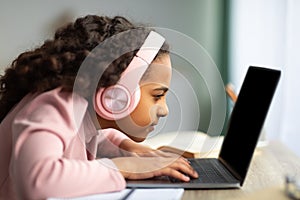 Youth and technology concept. Focused black schoolgirl using laptop computer, sitting at table too close to pc, side