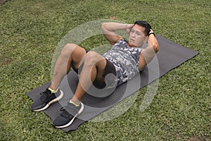 A youthful asian man does a set of ab crunches on a mat at his yard outdoors. Core workout