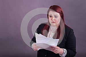 Youthful business woman looking down at stack of papers worried expression