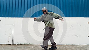 Youthful hipster dancing b-boy foot step at street with blue wall. Endeavor.