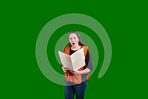 Youthful lady holding open file folder surprised expression on her face wearing a orange safety reflector vest