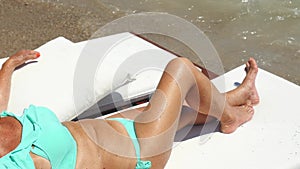 Youthful old woman in blue bikini sunbathing near the sea