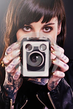 Youve been framed. Studio shot of a young tattooed woman holding a vintage camera.