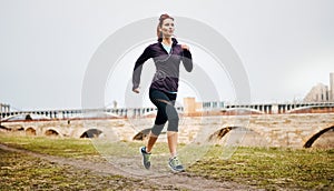 Youve gotta push yourself - no one else will. a sporty young woman listening to music while running alongside the city.