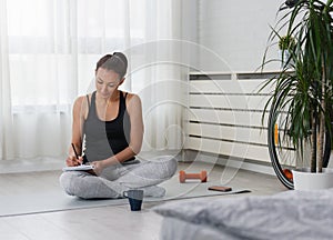 YouYoung sporty woman taking notes after exercise at home. New life resolutions list.