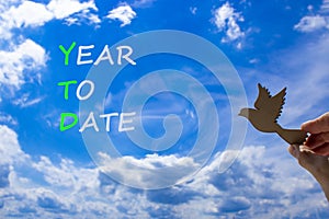 YTD year to date symbol. Concept words YTD year to date on beautiful blue sky clouds background. Wooden bird. Businessman hand. photo
