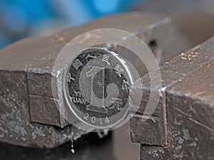 Yuan coin clamped in a metal vise. Currency under the onslaught, the concept of financial problems