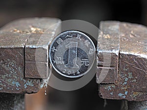 Yuan coin clamped in a metal vise. Currency under the onslaught, the concept of financial problems