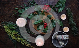 Yule winter solstice Christmas themed flat lay with branch of holly plant on a dark wooden table