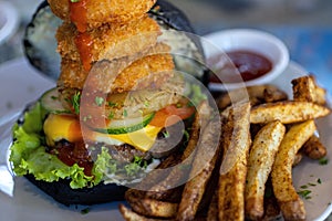 Yummy black burger with onion rings and fries