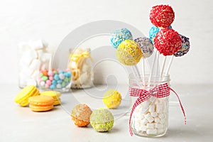 Yummy bright cake pops in glass jar full of marshmallows on table