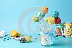 Yummy bright cake pops in glass jar full of marshmallows on table