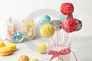 Yummy bright cake pops in glass jar full of marshmallows on table
