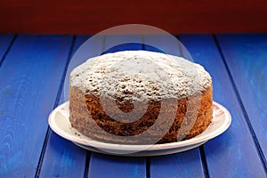 Yummy chocolate fruit cake with icing sugar on blue table