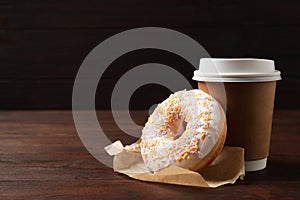 Yummy donut and paper cup on table against brown background, space for text