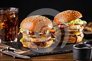 Yummy grilled chicken burger with double cutlet, fries and cola on a wooden table, side view.