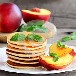 Yummy pancakes with sirup, nectarine and mint on a plate. Easy pancakes recipe for kids. Rustic style. Closeup