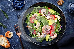 Yummy salad with fresh strawberry, shrimps, arugula, avocado and red onion, blue stone table. Fresh useful dish for healthy eating