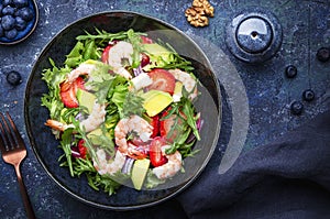 Yummy salad with fresh strawberry, shrimps, arugula, avocado and red onion, blue stone table. Fresh useful dish for healthy eating