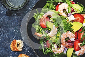 Yummy salad with fresh strawberry, shrimps, arugula, avocado and red onion, blue stone table. Fresh useful dish for healthy eating