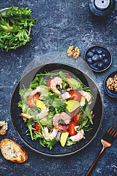 Yummy salad with fresh strawberry, shrimps, arugula, avocado and red onion, blue stone table. Fresh useful dish for healthy eating