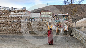 Tibetan monk praying in front of Mani stones at the Mani Temple Mani Shicheng wall with buddhist mantra Om Mani Padme Hum engrav