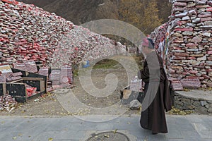 Tibetan monk walking in front of Mani stones wall with buddhist mantra Om Mani Padme Hum engraved in Tibetan in Yushu, China