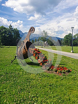 In Zakopane, a large wooden vase, a step full of small vases with colorful, red and orange flowers, on green grass. on the right,