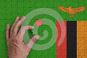 Zambia flag is depicted on a puzzle, which the man`s hand completes to fold