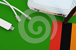 Zambia flag depicted on table with internet rj45 cable, wireless usb wifi adapter and router. Internet connection concept