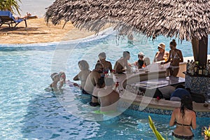 European tourists relaxing at the beach bar in the swimming pool at a tropical resort near the sea on the island of Zanzibar,