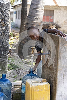 African boy fills the canister with tap water on a street in Zanzibar Island, Tanzania, East Africa