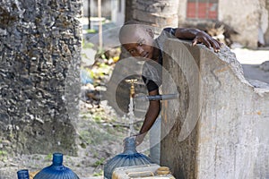 African boy fills the canister with tap water on a street in Zanzibar Island, Tanzania, East Africa