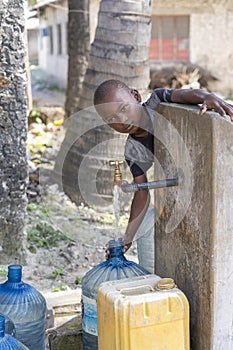 African boy fills the canister with tap water on a street in Zanzibar Island, Tanzania, East Africa