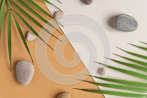 Zen flat lay composition with green leafs and stones. Tropical leaf and sea pebble on beige background. Spa or beauty template