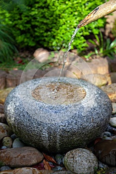 Zen fountain from the front made of granite stone that stands on large bricks with bamboo water inlet