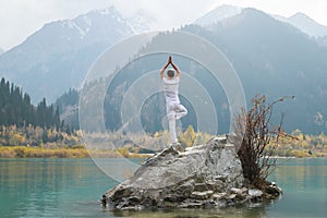 A zen man in white practices yoga in nature. Pose Vrikshasana or tree pose