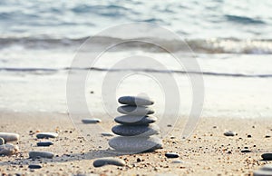 Zen pyramid of spa stones on the blurred sea background. Sand on a beach. Sea shores. Water waves texture. Left side of photo. Pla