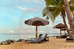 Zen scene of chaise lounge chairs on beach with thatched umbrellas and calm ocean