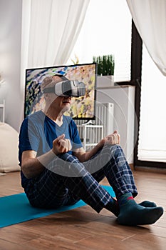 Zen senior man sitting on yoga mat in lotus position during pilates workout in living room