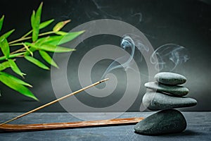 Zen spa basalt stones and green bamboo leaves and incense on black background.