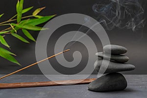 Zen spa basalt stones and green bamboo leaves and incense on black background.