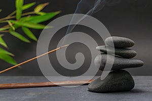 Zen spa basalt stones and green bamboo leaves and incense on black background.