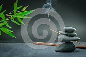 Zen spa basalt stones and green bamboo leaves and incense on black background.