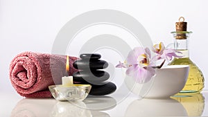 Zen spa stones, orchid flower in bowl, candle, bottle with oil and towel. Spa composition isolated on white background.