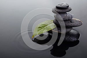 Zen stones in balanced pile and green leaf with water drops in water