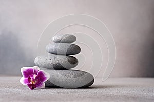 Zen stones and pink orchid flower on gray background as spa concept