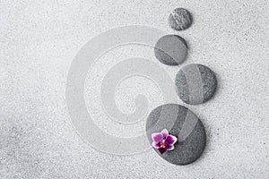 Zen stones and pink orchid flower on gray background as spa concept