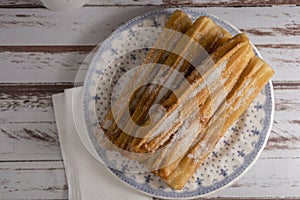 Zenital view of typical Hispanic churros filled with dulce de leche in a vintage plate on old boards. copy space photo
