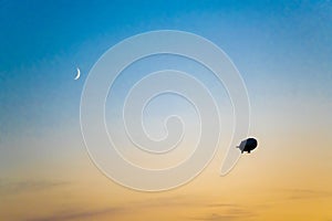 Zeppelin in evening sky with crescent moon. Airship in backlight in bright sky. Zeppelin in sky during sunset with crescent moon..